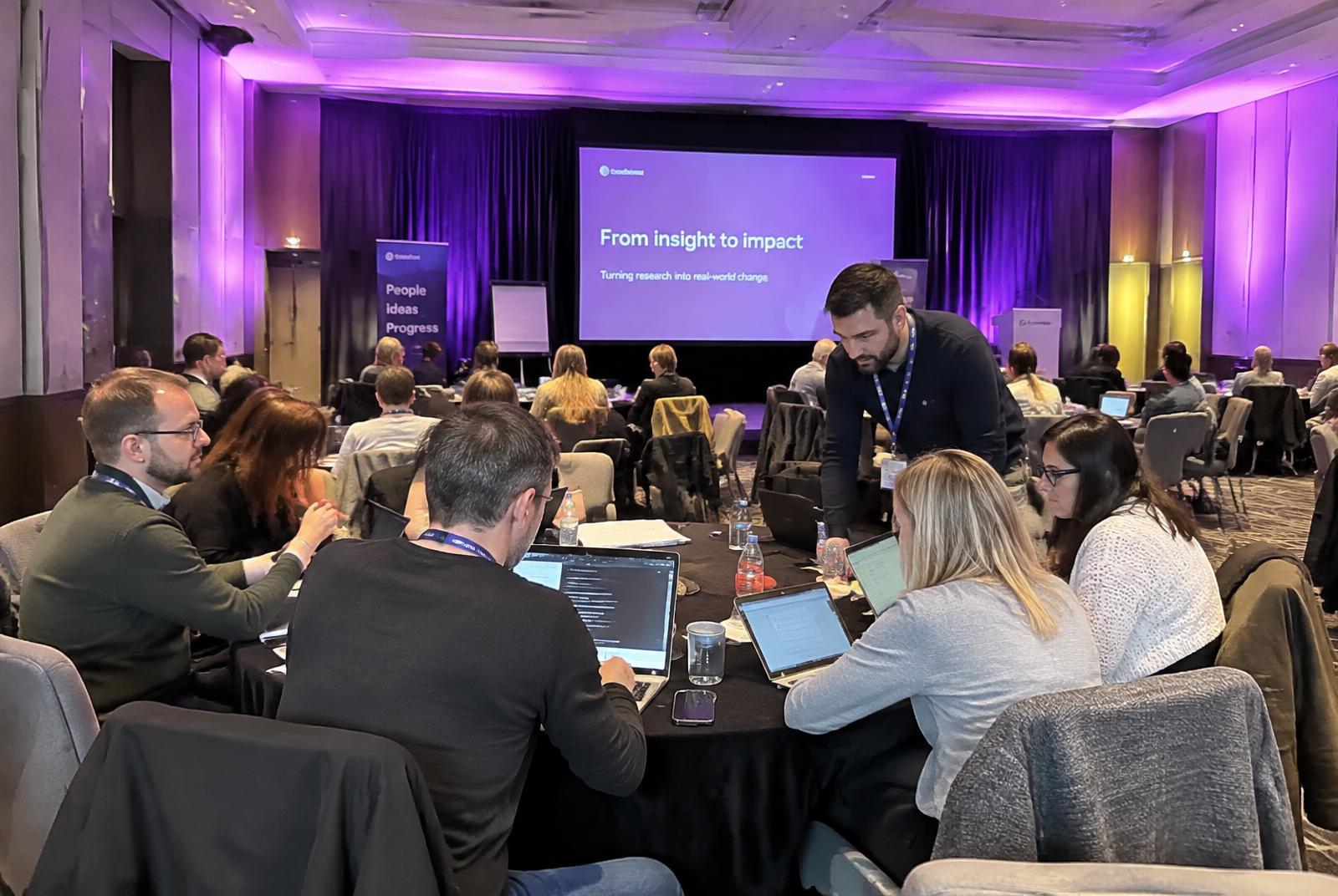 People working on laptops around a table at a Purple Bridge Media session